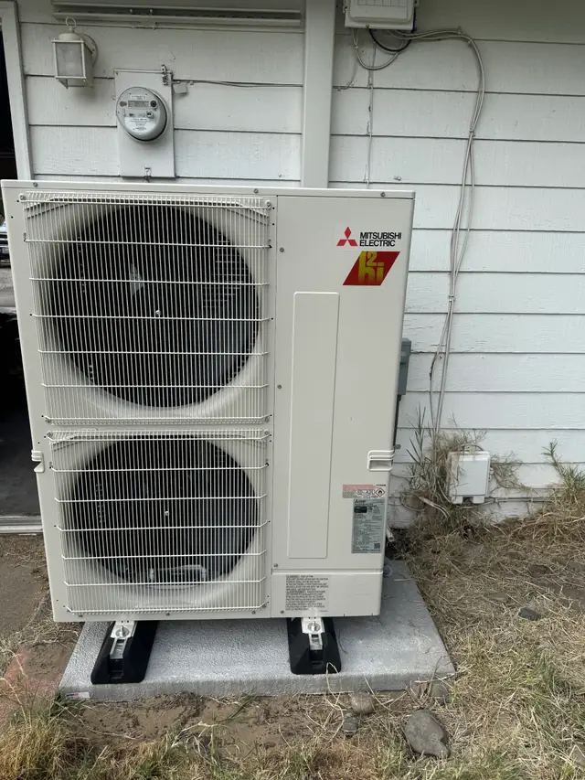 Mitsubishi Electric outdoor heat pump unit on its pad beside white siding in the Tri-Cities