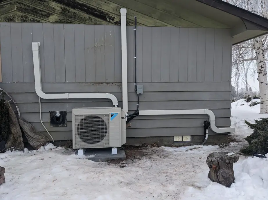 Daikin ductless outdoor unit with white line-set covers on grey siding, snow on the ground